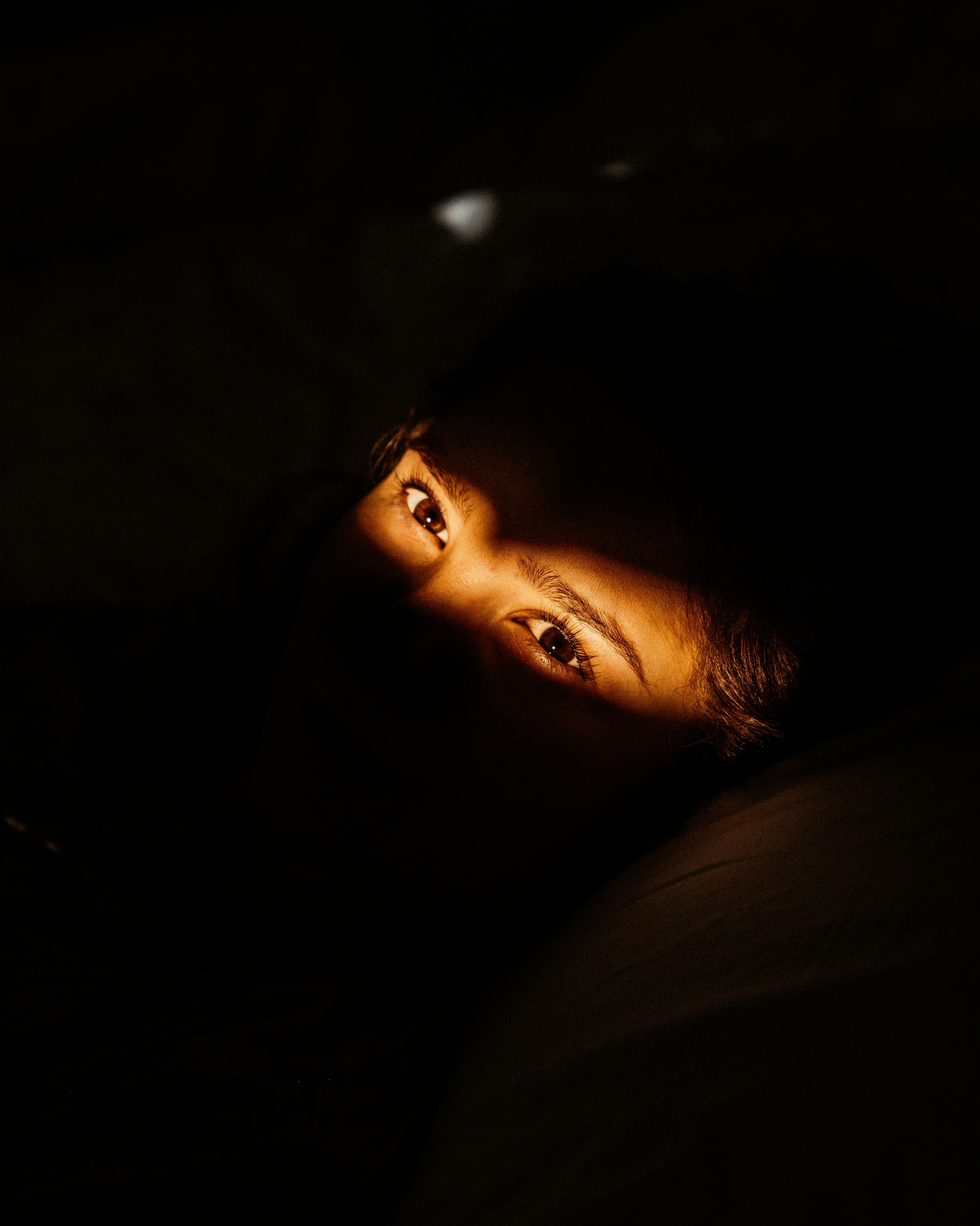 A person's eyes lit by a phone screen in the dark